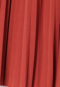 Faltenrock aus rostorangefarbenem Stoff, der vertikale Falten aufweist und für Textur sorgt. Das Material sieht glatt aus und hat einen leichten Glanz.