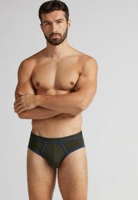 Ciemnozielone figi z niebieskimi akcentami, charakteryzujące się dopasowanym krojem i gładką fakturą. Pasek w talii jest markowy i stylizowany z kontrastowym wykończeniem.