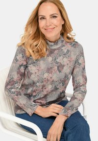 Langärmliges Oberteil im pink- und graufarbenen floralen Muster mit hohem Kragen, aus weichem Stoff, kombiniert mit dunkelblauen Jeans.