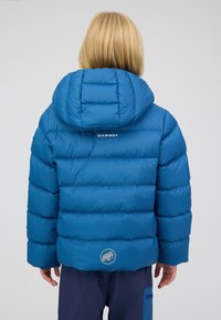 Blaue Pufferjacke mit horizontalem Steppmuster, angenommener Kapuze und Mammut-Logo auf dem Rücken. Weiche Textur mit glänzendem Finish.