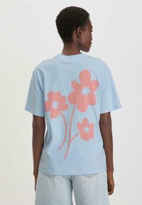 Blauwe T-shirt met korte mouwen, voorzien van grote roze bloemgraphics op de achterkant. Gemaakt van zacht materiaal met een relaxte pasvorm en een ronde hals.