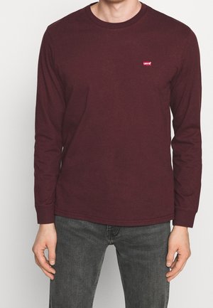 Chemise à manches longues bordeaux en coton avec un col rond. Présente un petit logo rouge Levi's sur la poitrine. Portée avec un jean gris.