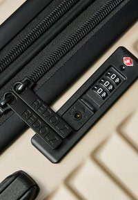 Nahaufnahme eines beigen Koffers mit schwarz doppeltem Reißverschluss und integriertem TSA-Kombinationsschloss, das auf 0-0-0 eingestellt ist, mit dem Markennamen Redolz.