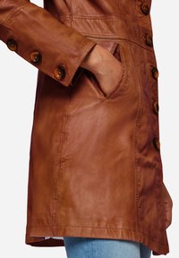 Brun skinnjacka med stora knappar, knappslå, sidofickor och en slät textur, med en skräddarsydd silhuett.