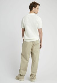 Polo en maille blanche à manches courtes, associé à un pantalon large beige clair, avec des détails de couture visibles et une texture douce.