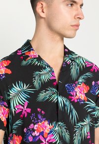 Schwarzes Kurzarmhemd mit einem lebhaften Blumen- und tropischen Blattmuster in Pink, Lila und Türkis, mit einem spitzen Kragen und Knopfverschluss.