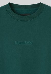 Sweat à capuche teal avec un col ras du cou en côtes et un texte brodé subtil "légendaire" à l'avant. Texture de tissu lisse, design décontracté.