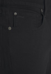 Jeans de mezclilla negra con un diseño clásico, con costuras visibles, cierres de botón y un pequeño logotipo en el bolsillo frontal.