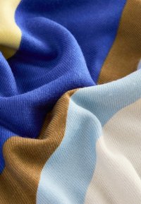 Tissu tricoté avec un motif ondulé dans des couleurs bleu, jaune, marron et bleu clair, avec une texture douce et des coutures visibles.