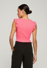 Top aderente rosa con maniche arricciate, realizzato in un tessuto elastico. Il retro presenta un collo rotondo e un design corto, abbinato a pantaloni neri.