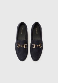 Marineblå suede loafers med gulldetaljer, rund tå og sydd detaljering langs kantene. Myk tekstur og slip-on design.