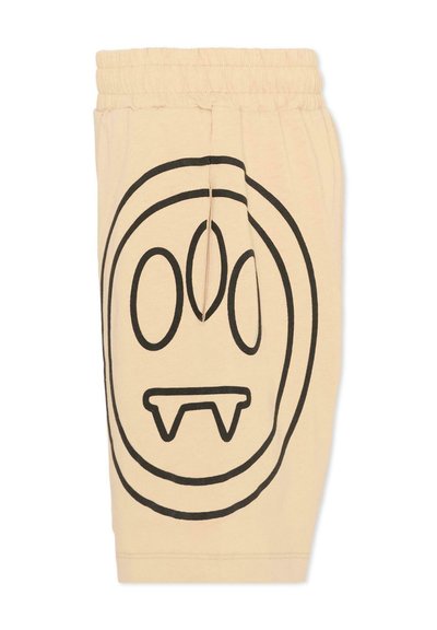 Pantalones cortos beige con cintura elástica, con un gran rostro abstracto delineado en negro que presenta ojos ovalados y colmillos afilados en una pierna.