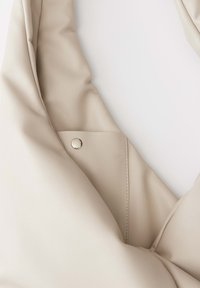 Borsa di pelle beige con un design morbido e soffice, caratterizzata da un bottone a pressione visibile e una cucitura pulita lungo i bordi.