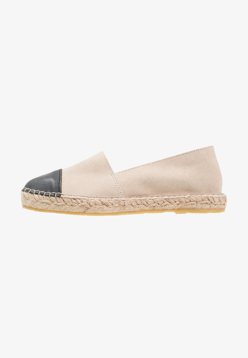 Espadrille beige avec bout rond noir, semelle en jute tissée et semelle extérieure plate en caoutchouc, vue de côté sur fond blanc.