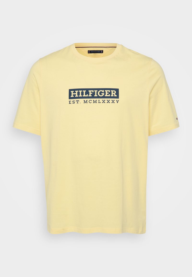 Żółta bawełniana koszulka z krótkim rękawem, z granatowym prostokątnym logo na piersi, które brzmi "HILFIGER EST. MCMLXXXV".