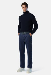 Dunkelblauer, gerippter Rollkragenpullover, dunkelblaue Cargo-Hosen mit Seitentaschen und weiße Sneakers, ergänzt durch einen schwarzen Gürtel mit Metallakzenten.