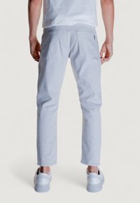 Pantalones de mezclilla en gris claro con un ajuste slim, que cuentan con dos bolsillos traseros y un diseño liso, combinados con zapatillas blancas.