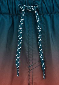 Tamsiai žaliai mėlynas raištelis su baltomis detalėmis, įveržtas per juosmens juostelę, pagamintą iš audinio, kuriame matomas gradientas nuo tamsiai žalios iki raudonai rudos spalvos.