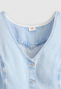 Camicia in denim blu chiaro con bottoni, caratterizzata da una scollatura a V, bottoni argentati e cuciture standard. Etichetta Levi's visibile all'interno del collo.