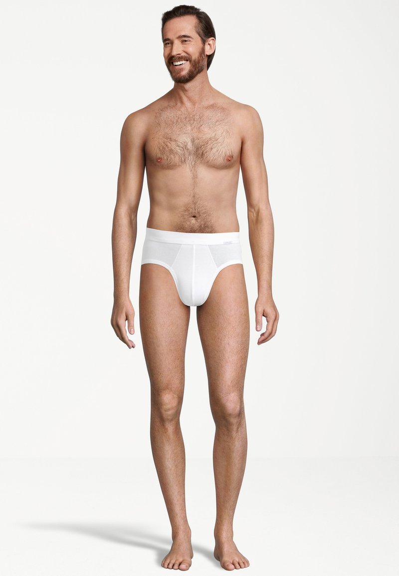 Slip di cotone bianco, design a vita media, texture liscia, cinturino elastico con cuciture minimaliste, indossato da una figura maschile in piedi.