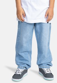 Svetle modré džínové kalhoty s volným střihem, zdobené viditelnými švy. V kombinaci s šedými teniskami, které zvýrazňují bílé tkaničky a mentolovou podrážku.