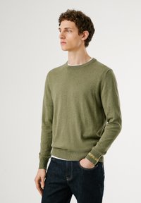 Suéter de mezcla de lana verde con cuello redondo, puños acanalados y dobladillo. Presenta una textura sutil y una marca en el puño.