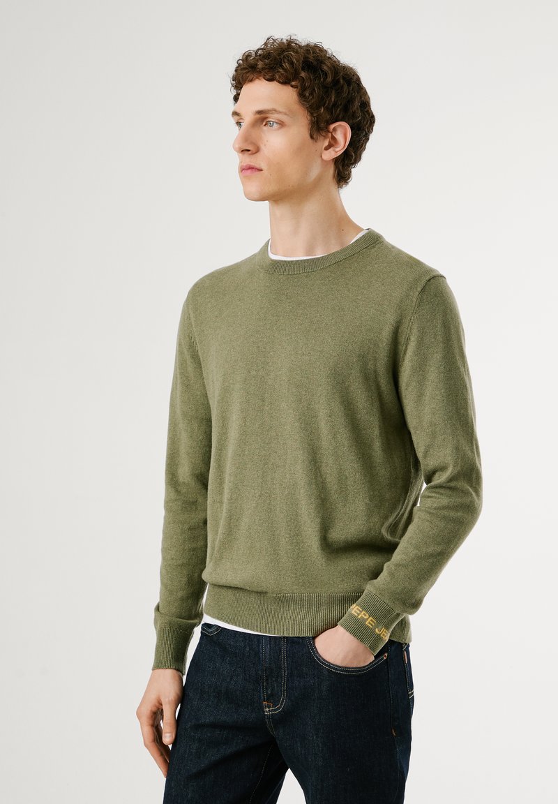 Maglione verde in misto lana con scollo tondo, polsini e orlo a coste. Presenta una trama sottile e un marchio sul polsino.