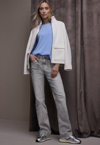 Witte fleece ritsjas over een lichtblauw shirt, gecombineerd met lichtgrijze spijkerbroeken en metallic zilveren sneakers. Eenvoudig ontwerp, ontspannen pasvorm, basisteksturen.