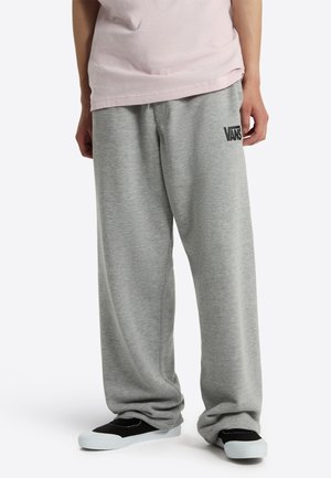 Person iført løse grå joggingbukser med sort Vans-logo og sorte slip-on sko med hvide såler.