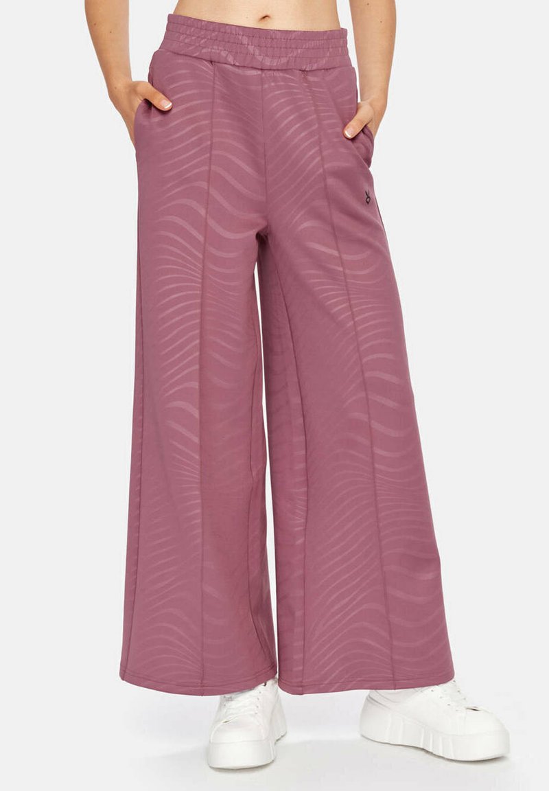 Wijde broeken in gedempt mauve met golvend textuurpatroon, elastische tailleband en zijzakken, gecombineerd met witte platform sneakers.