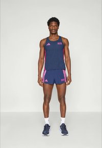 Sportliches Outfit für Herren mit einem ärmellosen Oberteil in Marineblau und pinken Akzenten sowie passenden Shorts. Kombiniert mit weißen Socken und dunklen Turnschuhen.