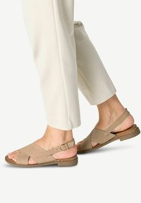 Sandales en cuir beige avec des brides croisées et une boucle de cheville réglable, dotées d'une semelle plate et d'un accent en liège texturé.