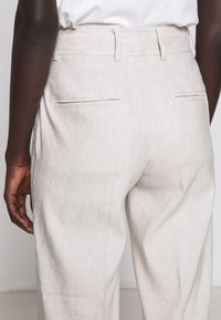 Ljust beige byxor i ett strukturerat tyg. Har en skräddarsydd passform, två bakfickor och bältesöglor i midjan.