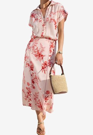 Bloemrijke jurk in zachtroze met rode patronen, met een kraag, korte mouwen en zijsplitten; gecombineerd met een geweven handtas en platte sandalen.