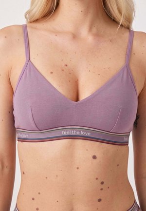 Kobieta nosząca fioletowy biustonosz bralette z cienkimi ramiączkami i paskiem z napisem "feel the love" na wysokości klatki piersiowej.