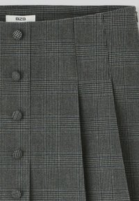 Jupe à carreaux grise avec une texture lisse, dotée d'une taille haute, de multiples boutons et de plis nets créant des lignes structurées.