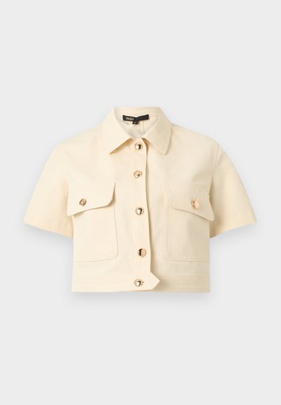 Κοντομάνικο μπεζ πουκάμισο με γιακά, μπροστινά χρυσά κουμπιά και δύο τσέπες στήθους με καπάκι και κουμπί, σε απλό φόντο.