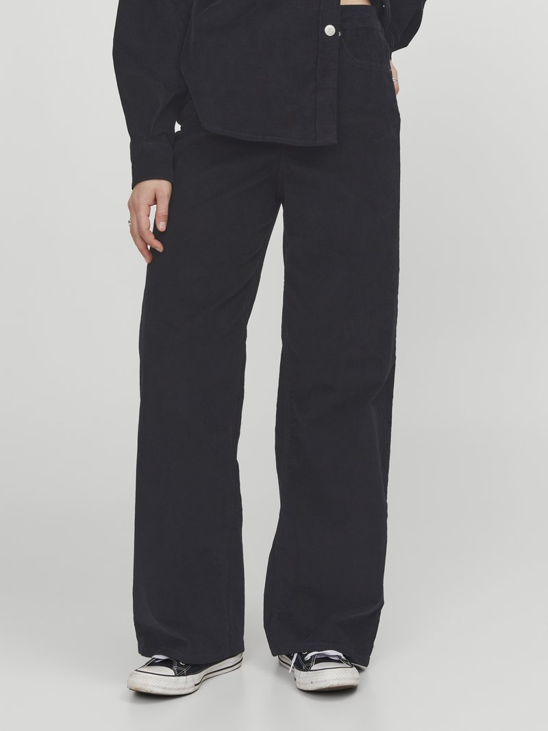 Wide-leg black corduroy pants with textured fabric; features front pockets and an elastic waistband, complemented by low-top sneakers.