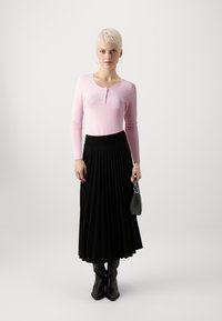 Langærmet lyserød bluse med henley-udskæring, parret med en sort plisseret nederdel. Sorte hæle og en lille sort håndtaske fuldender looket.