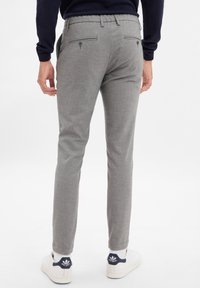Pantaloni grigi a fantasia con vestibilità slim, dotati di tasche posteriori e una texture liscia, abbinati a sneakers bianche.
