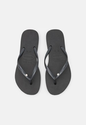 Chanclas negras con plantilla de goma texturizada y arnés plano. Presentan tiras finas con un acento plateado en una de las tiras y detalle del logo.