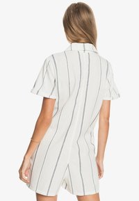 Combinaison à manches courtes en tissu blanc avec des rayures verticales bleu foncé, dotée d'un col et d'un détail d'ouverture à l'arrière.