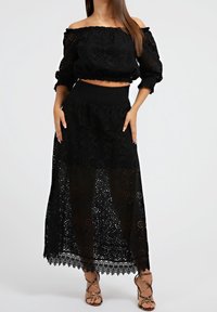 Schwarzes Zweiteiler-Outfit mit einem Schulterfreien Cropped-Top und einem langen, durchsichtigen Rock mit floralen Ausschnittmustern und gewelltem Saum.