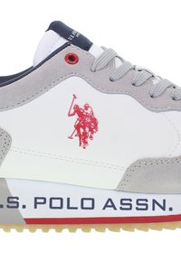 Zapatilla blanca con detalles en gamuza gris, logotipo rojo y suela de goma gris. Presenta una lengüeta de tejido azul y la marca "U.S. Polo Assn."