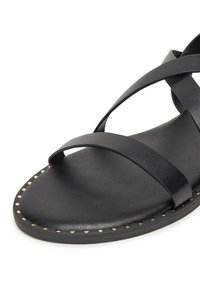 Czarne sandały z krzyżującymi się paskami wykonanymi z gładkiej skóry. Posiadają płaską podeszwę z detalami w postaci złotych ćwieków wzdłuż krawędzi. Minimalistyczny design.