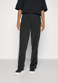 Black athletic pants with a straight leg design, featuring white side stripes and an elastic waistband. Worn with black sneakers.