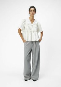Weiße Baumwollbluse mit puffierten Ärmeln und gerafften Details, kombiniert mit locker sitzenden grauen Jeans. Beide Kleidungsstücke haben eine entspannte Passform.
