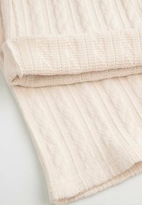 Jasnobeżowy dziergany koc z teksturowanym wzorem z podniesionymi liniami i detalami warkoczowymi, złożony na jednym brzegu. Miły i przytulny wygląd.