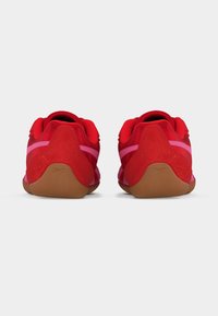 Ζεύγος κόκκινων αθλητικών παπουτσιών με ροζ ρίγες και καφέ σόλες, εμφανιζόμενα από πίσω σε λευκό φόντο.