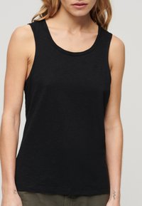 Zwarte mouwloze tanktop van zacht stof met een ronde halslijn en een lichte glans; heeft een klein logo in de bovenste linkerhoek.